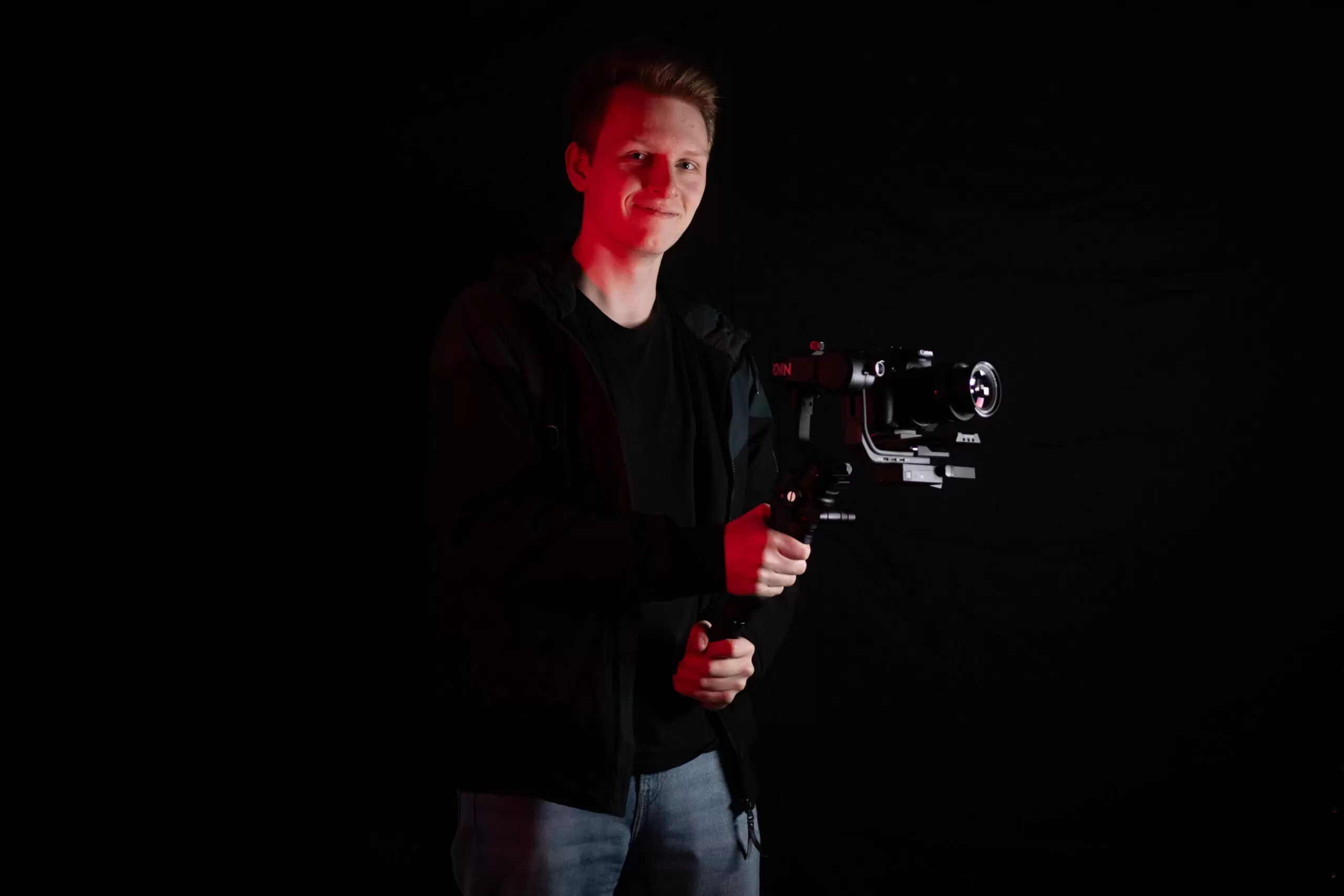 David Melüh von funeralhomefilms hält ein Kamera-Gimbal und lächelt in die Kamera. Er wird von rotem Licht beleuchtet.