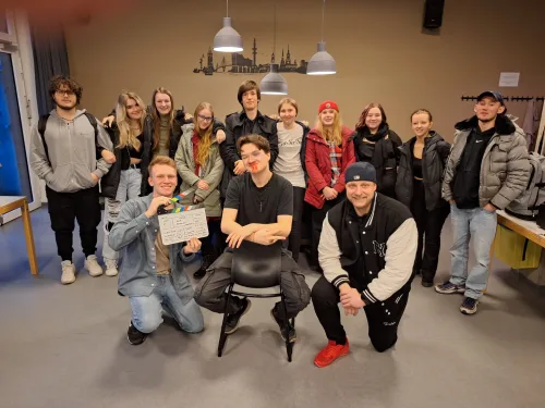     Großes Gruppenfoto der Filmcrew und Darsteller vom Set des Films Leidenschaft, die gemeinsam in einem Raum posieren. Eine Person im Vordergrund hält eine Filmklappe, während eine andere Person mit Kunstblut geschminkt ist.