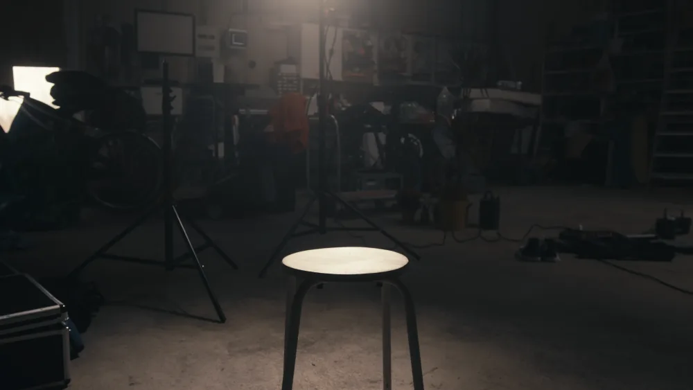 Produktionsteam bereitet sich in einer Werkstatt-Atmosphäre auf den Dreh vor, Filmtechnik und Requisiten sind im Raum verteilt.